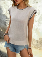 Sleeveless beige knit sweater with black trim, paired with distressed denim shorts, outdoor setting.