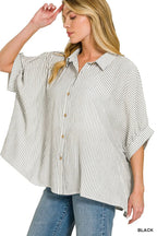 Woman wearing a relaxed-fit black and white striped button-up shirt with rolled sleeves and blue jeans.