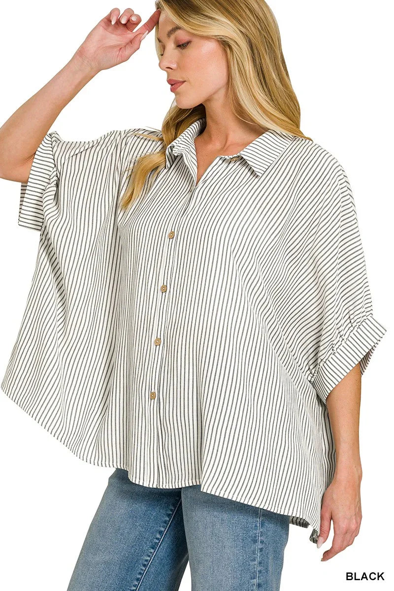 Woman wearing a relaxed-fit black and white striped button-up shirt with rolled sleeves and blue jeans.