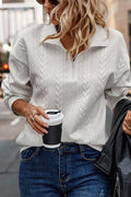 Woman wearing white cable knit pullover sweater and blue jeans holding coffee cup on city street