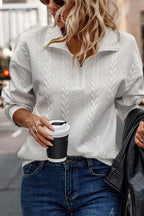 Woman wearing white cable knit pullover sweater and blue jeans holding coffee cup on city street