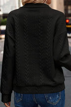 Back view of a woman wearing a textured black sweater with chevron knit pattern and blue jeans.