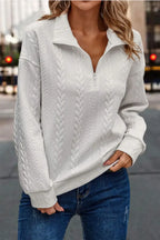 Woman wearing a white cable knit quarter-zip sweater with blue jeans outdoors