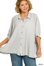 Woman wearing an oversized black and white striped button-up shirt with cuffed sleeves and blue jeans