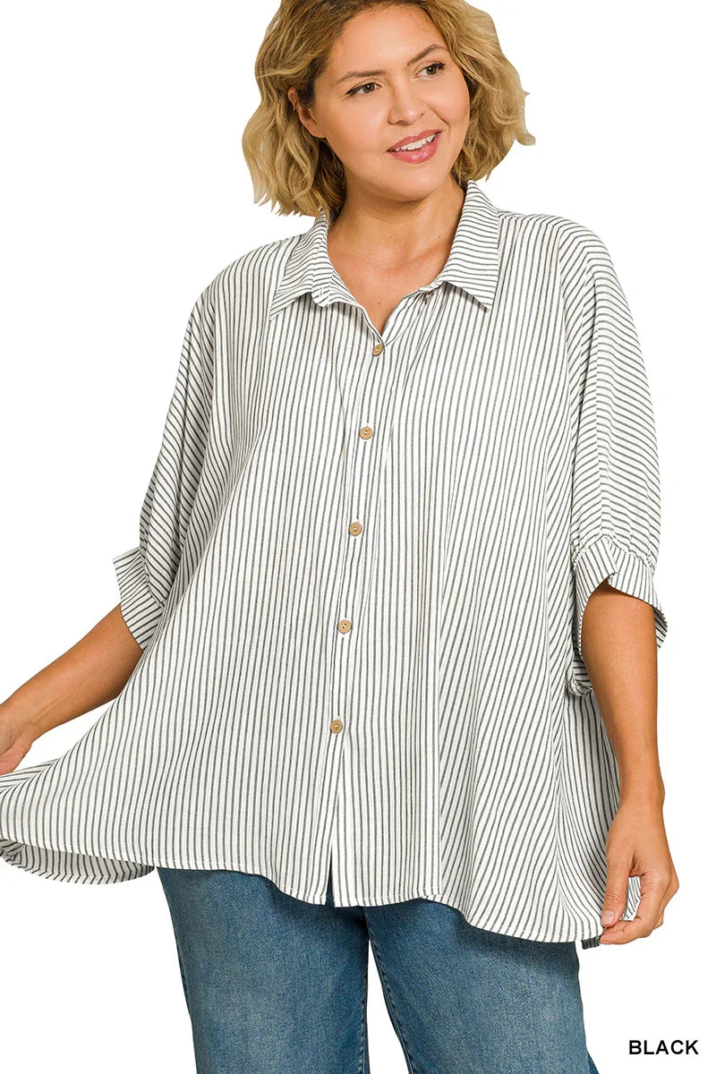 Woman wearing an oversized black and white striped button-up shirt with cuffed sleeves and blue jeans