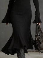 Close-up of a black ribbed knit dress with flared sleeves and ruffled hem, contemporary style