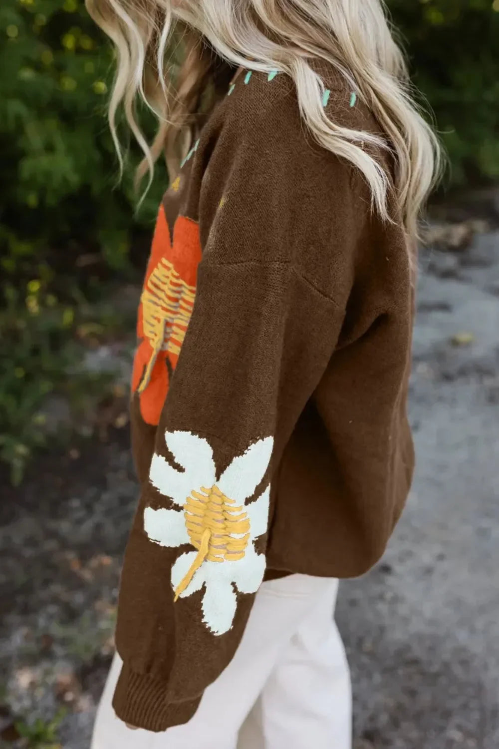 Brown knit sweater with bold floral patterns, worn outdoors by a woman with blonde hair