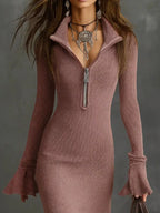 Woman wearing a fitted mauve ribbed knit dress with zipper front and bell sleeves, styled with layered silver jewelry.