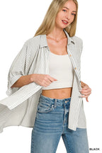 Woman wearing a black striped oversized shirt over a white crop top and blue high-waisted jeans