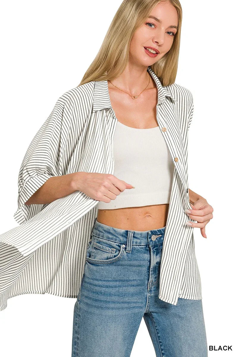 Woman wearing a black striped oversized shirt over a white crop top and blue high-waisted jeans