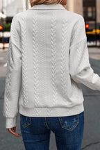 Woman wearing a white textured knit sweater and blue jeans outdoors