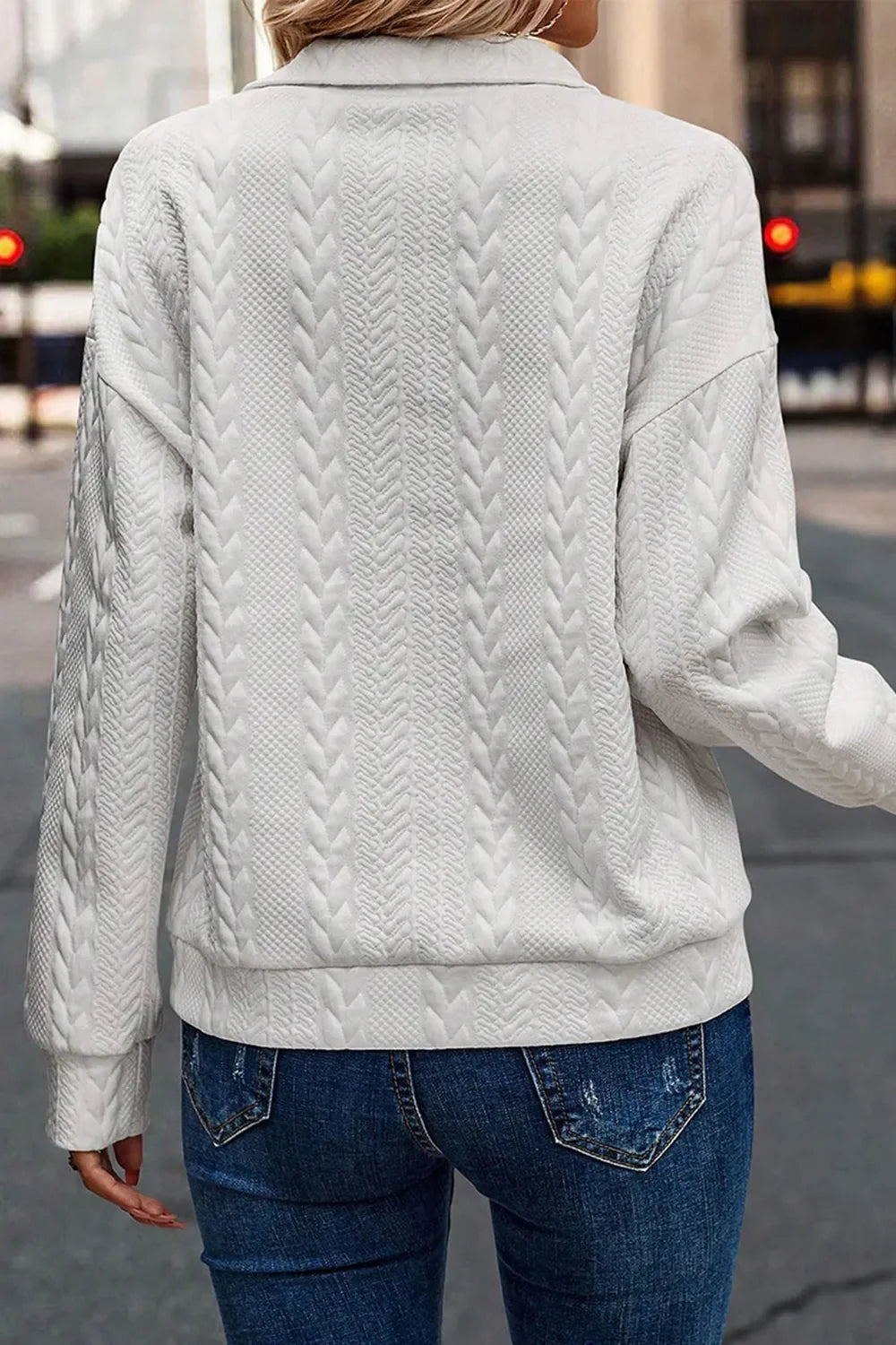 Woman wearing a white textured knit sweater and blue jeans outdoors