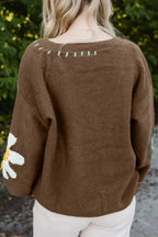 Brown knit sweater with floral sleeve detailing and mint green embroidered accents, outdoor setting
