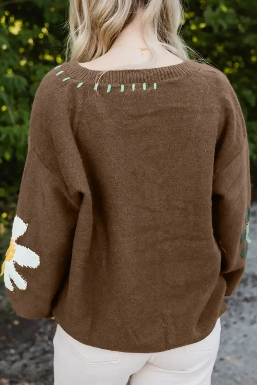 Brown knit sweater with floral sleeve detailing and mint green embroidered accents, outdoor setting